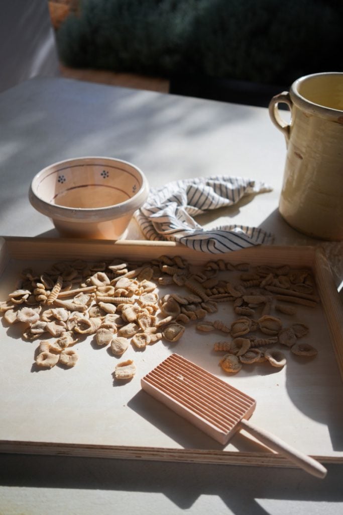 A local artisan hand-rolling traditional orecchiette pasta on a wooden table.