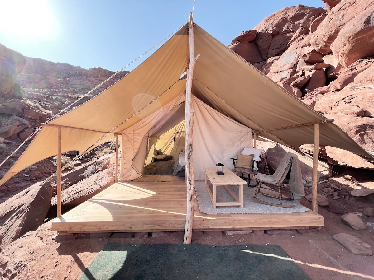 A luxury glamping tent on a wooden platform set against a backdrop of red desert cliffs.