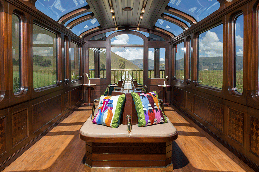 A train observation car with large windows and an outdoor viewing deck looking out at green mountains.