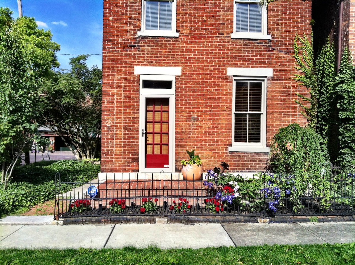 A charming brick cottage with a bright red door and lush green ivy in German Village.