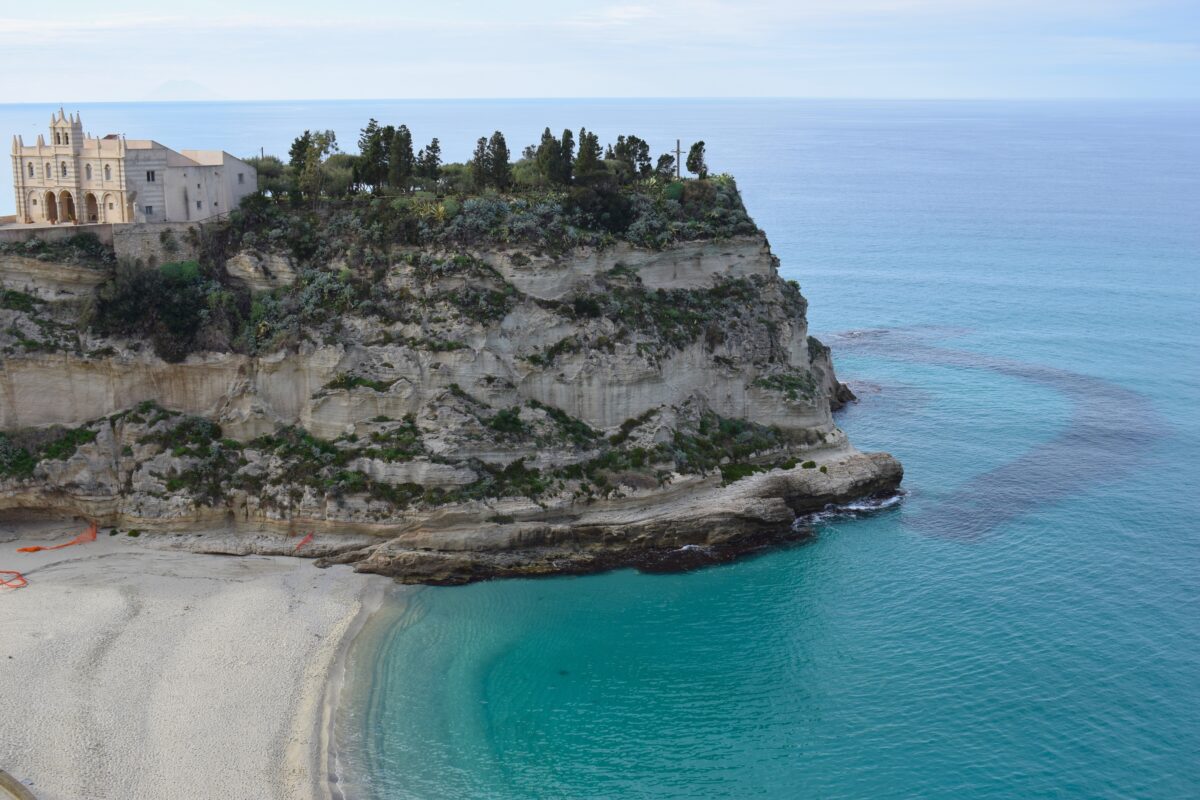 The sandy shore of Rotonda Beach in Tropea with the historic town perched on a cliff in the background.