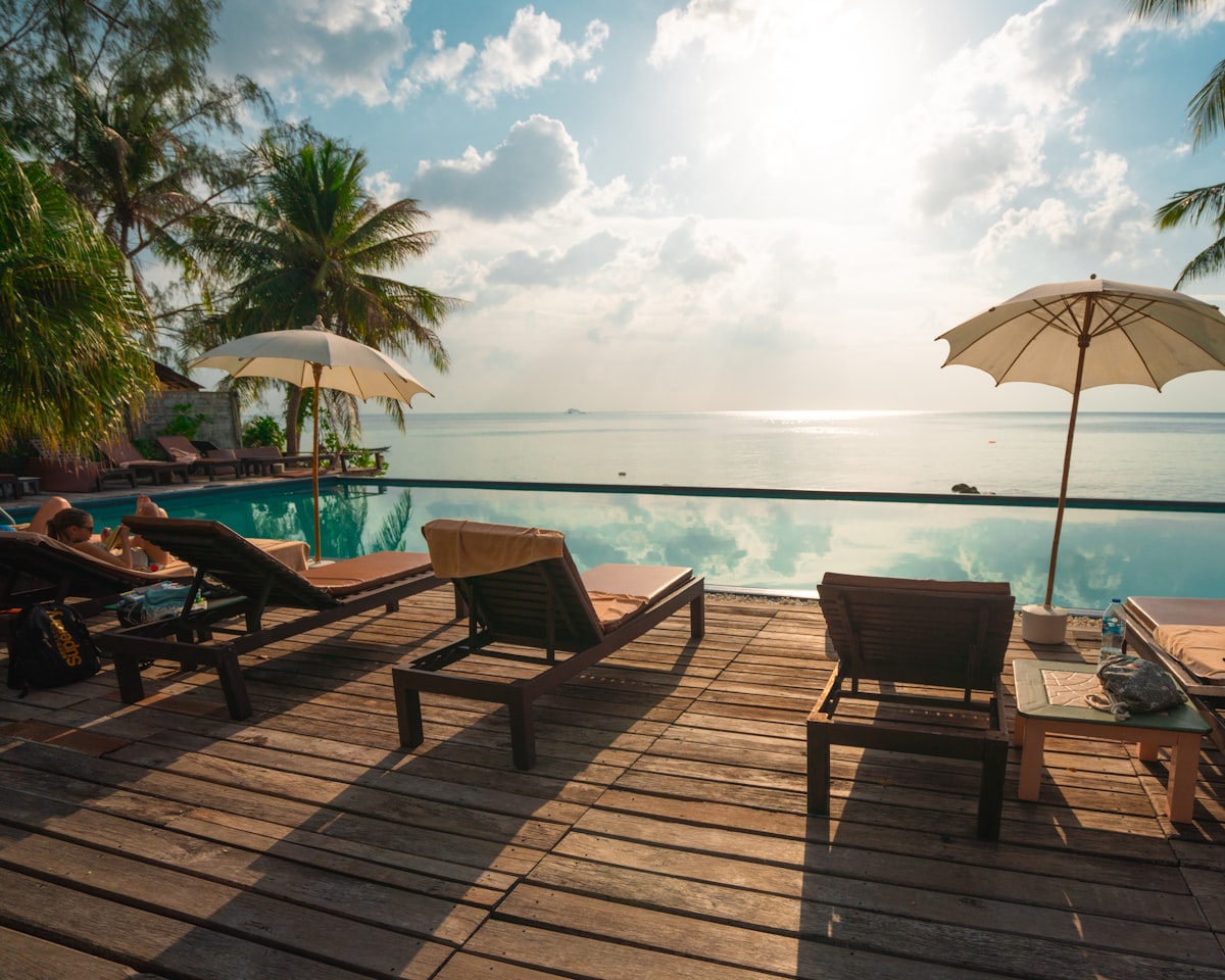A tranquil luxury resort swimming pool surrounded by palm trees under a bright blue sky.