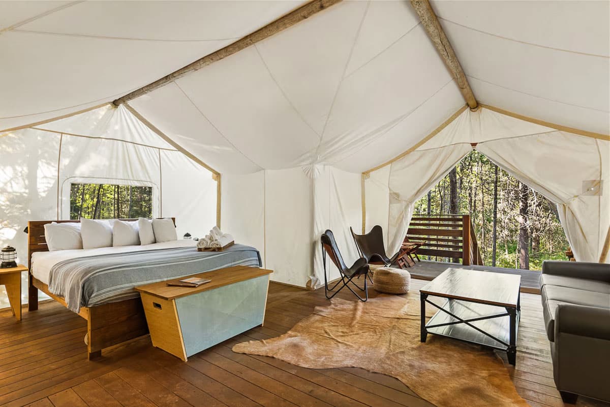 Interior of a luxury glamping tent featuring a large plush bed, wooden furniture, and canvas walls.
