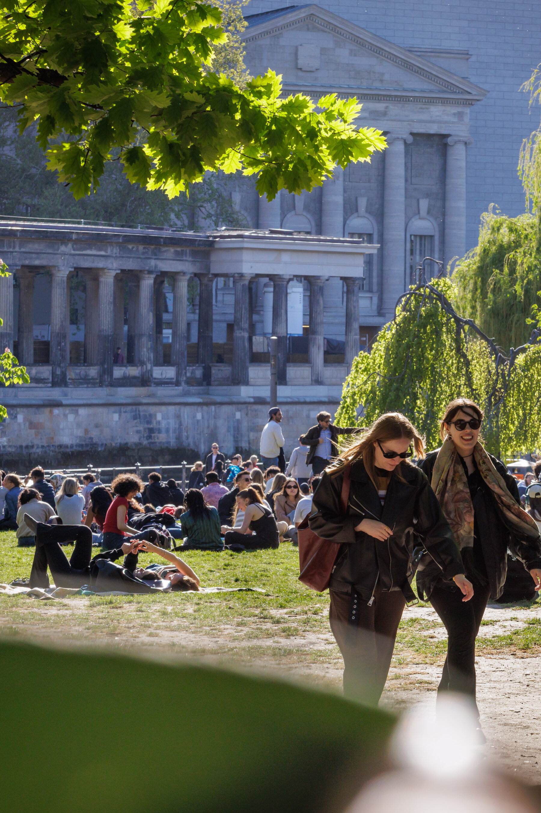 People sitting on the grass in James-Simon-Park with the historic buildings of Museum Island in the background.