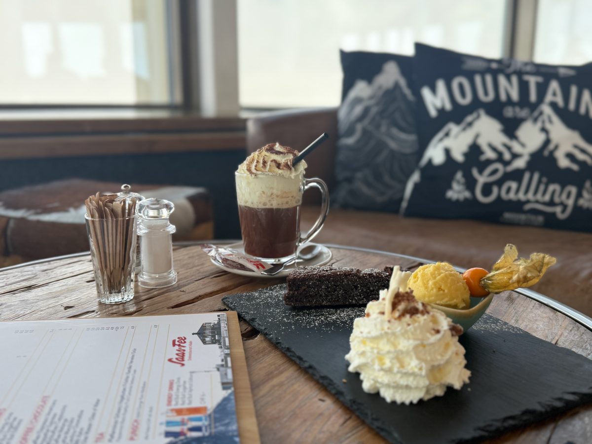 A dessert plate on a table at the Allalin revolving restaurant with snowy mountains visible through the window.