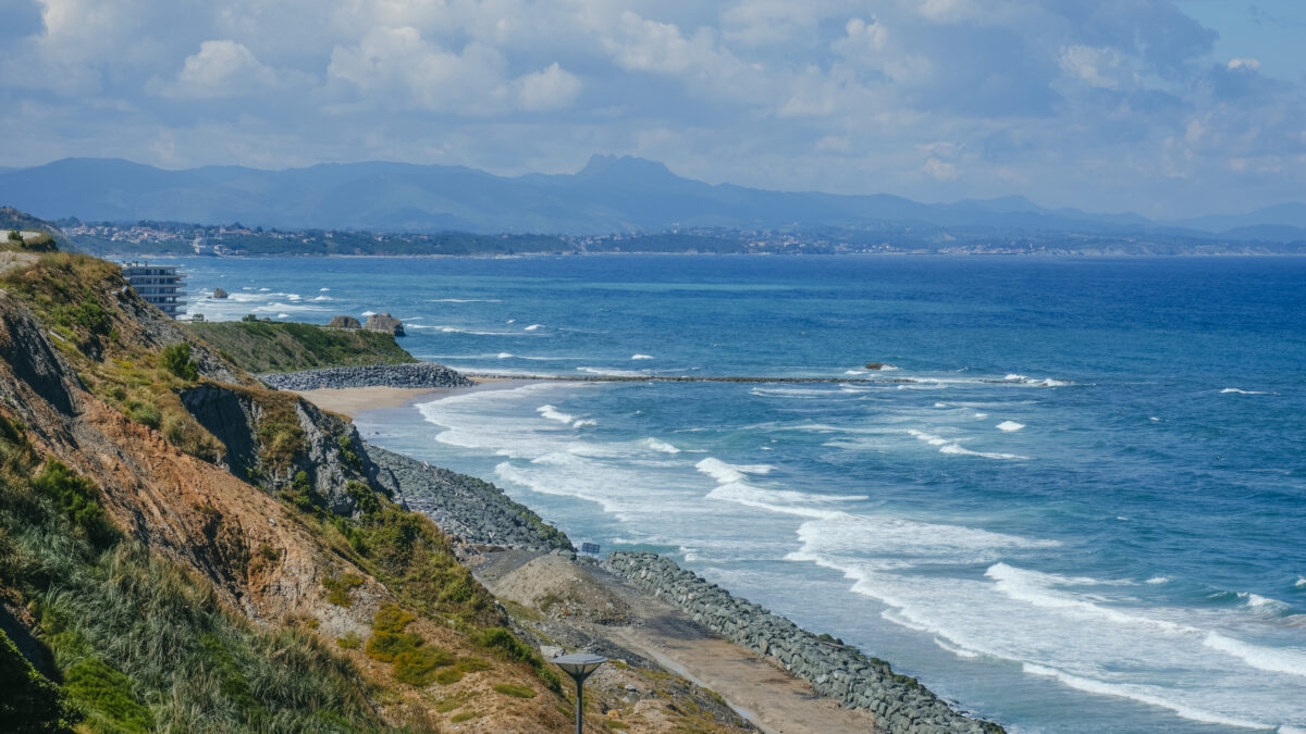 Surfers catching waves at Côte des Basques in Biarritz with the historic Villa Belza on the horizon.