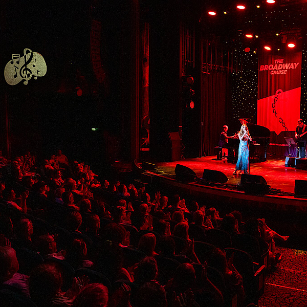 Broadway actors performing a musical number on a large shipboard stage with professional lighting.