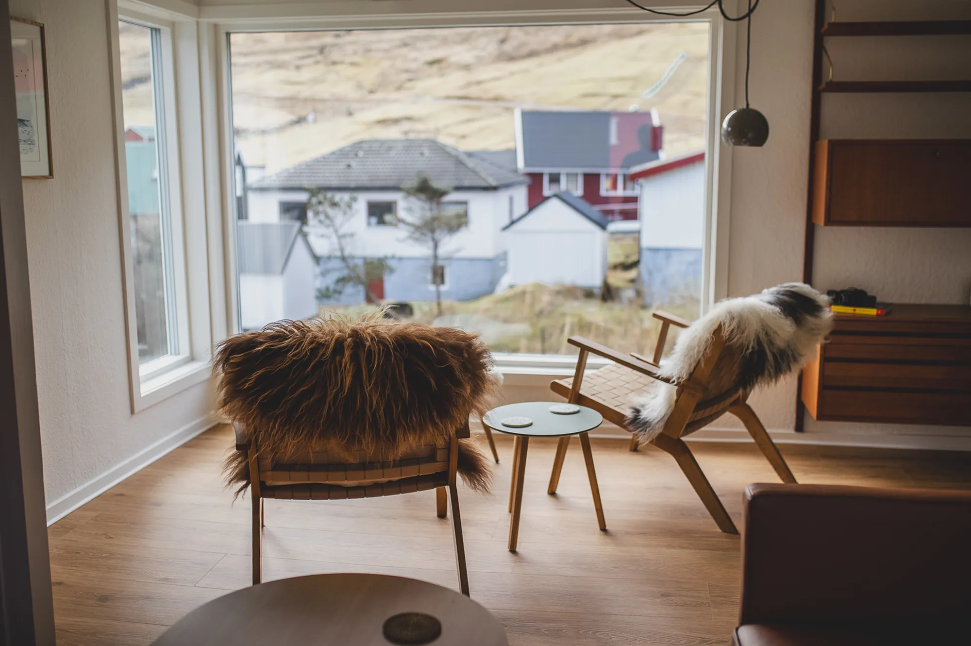 An interior view of a Faroese living room with large windows looking out onto a rural village.