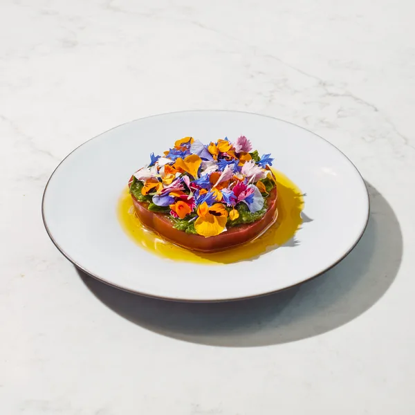 An artfully plated gourmet tomato and herb dish served in a contemporary restaurant setting.