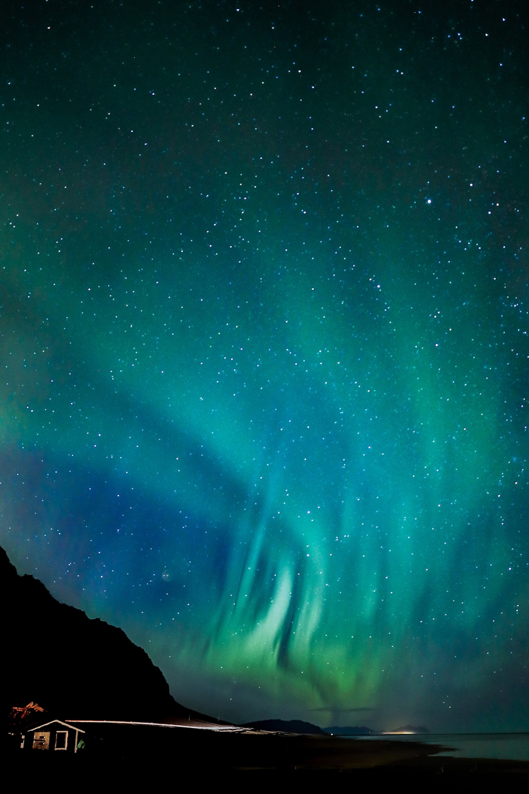 A wide-angle shot of the green aurora borealis stretching across a starry mountain sky.