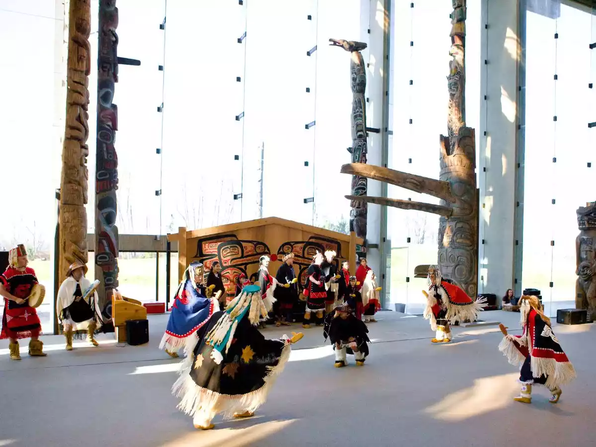 Indigenous performers in vibrant traditional regalia dancing during a museum ceremony.