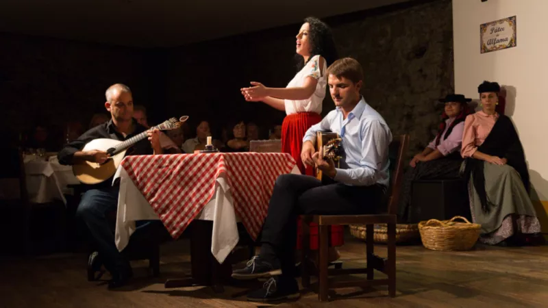 A female singer performing Fado music accompanied by acoustic guitarists in a dim restaurant.