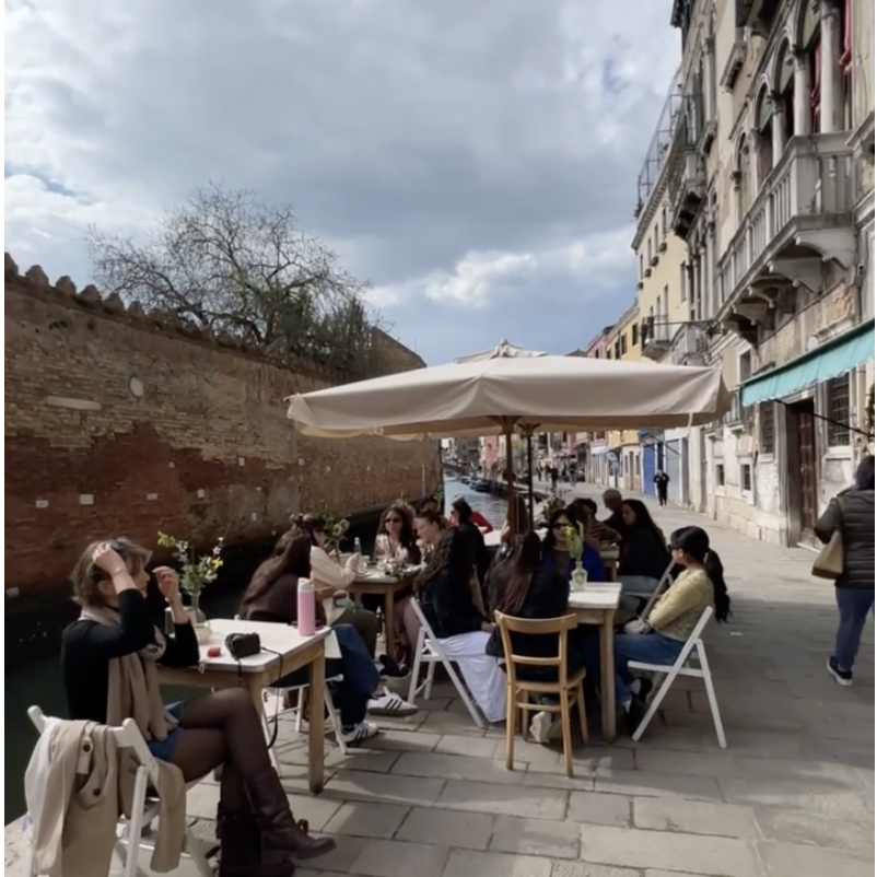 Diners enjoying food at tables set up alongside a picturesque canal.