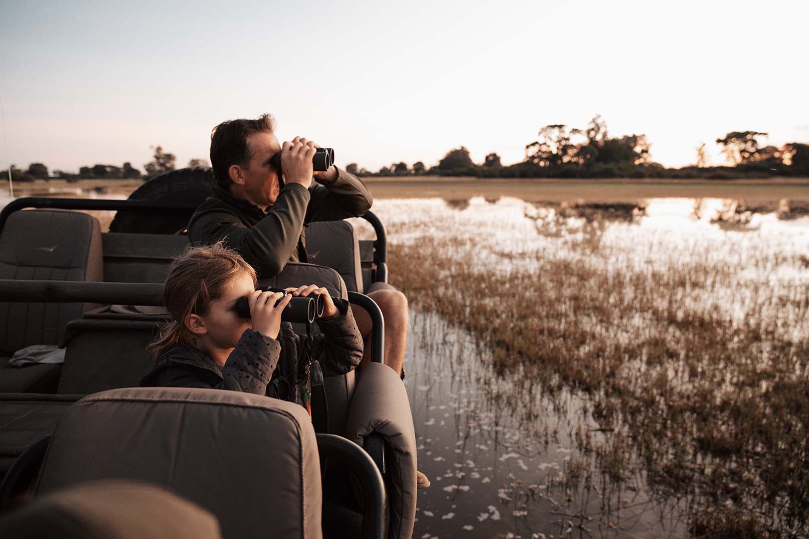 A multi-generational family sitting in an open-top safari vehicle watching wildlife.