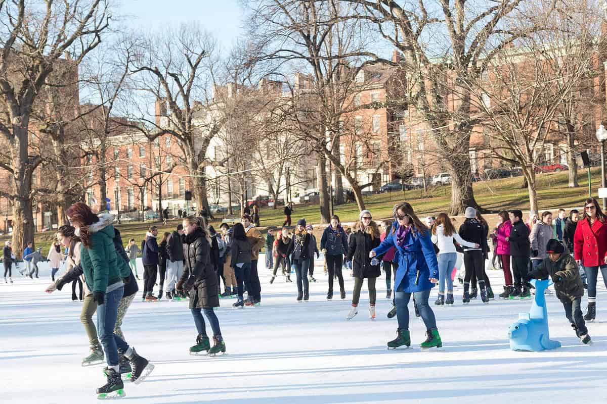 Ice skaters circling the rink at Boston Common Frog Pond surrounded by winter trees.