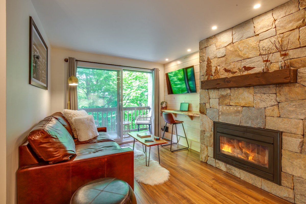 A cozy living room featuring a large stone fireplace, leather armchairs, and rustic wooden accents.