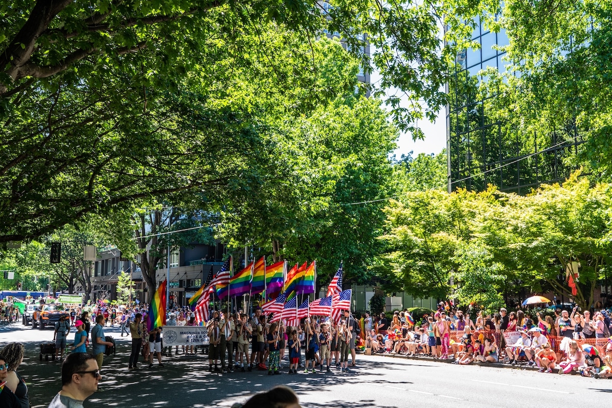 Crowds cheering at a colorful Seattle Pride parade in the city center.