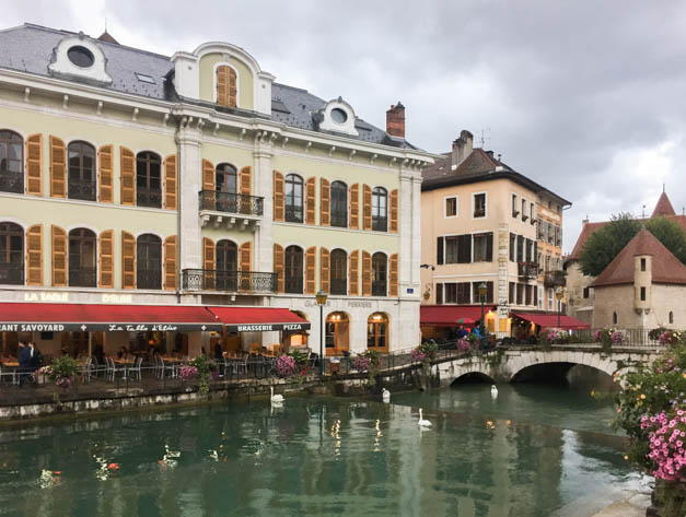 Colorful medieval buildings lining a quiet canal with stone bridges in Annecy.