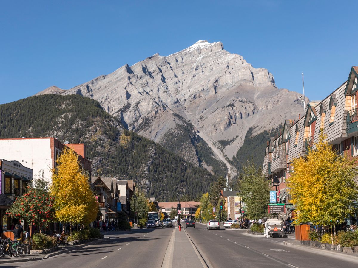Crowded Banff Avenue with many tourists and a mountain backdrop in summer.