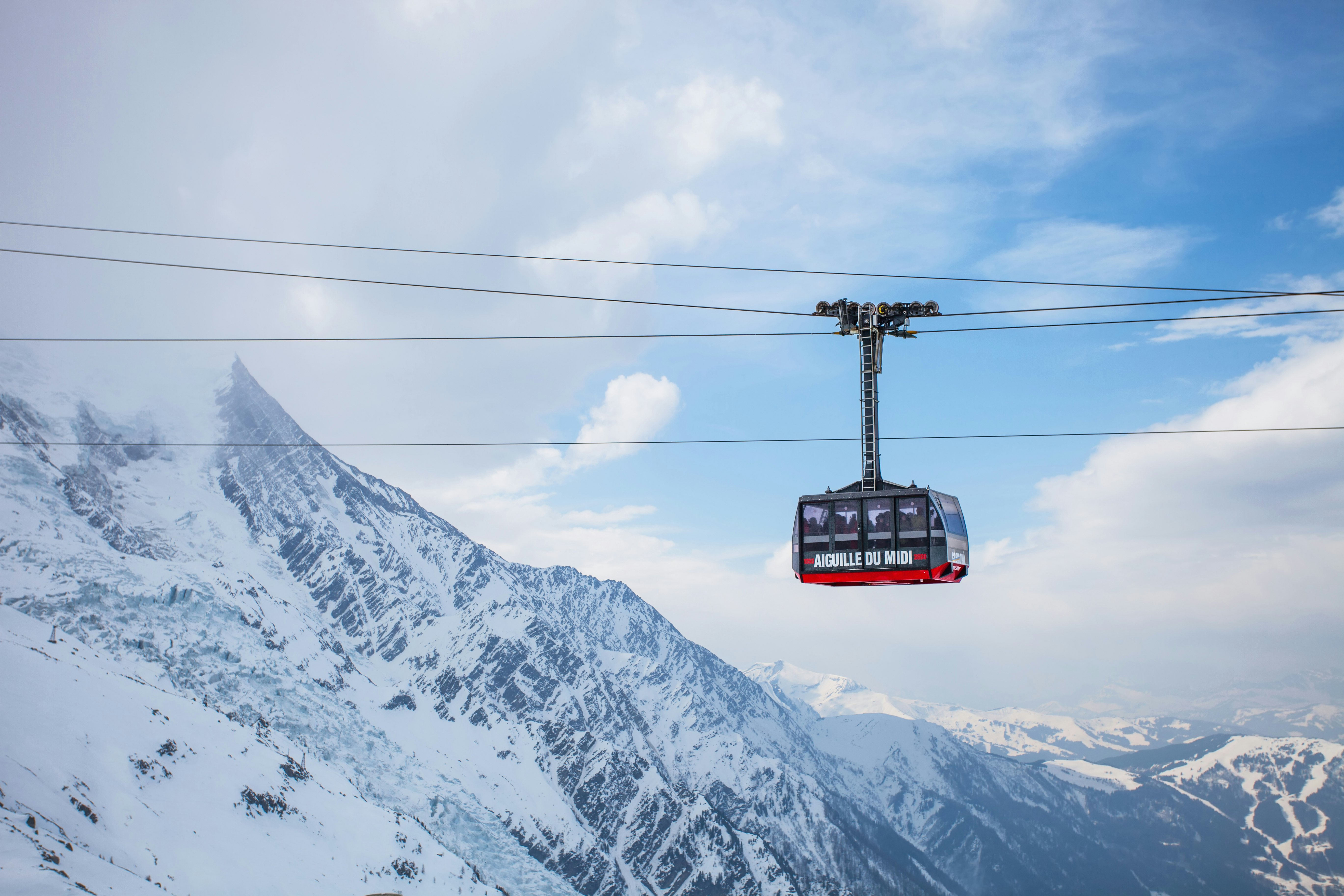 A modern cable car gondola ascending over vast, snowy alpine slopes.