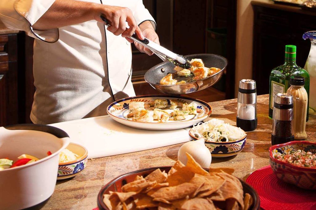 A private chef providing a culinary cooking class to a guest in a luxury villa kitchen.