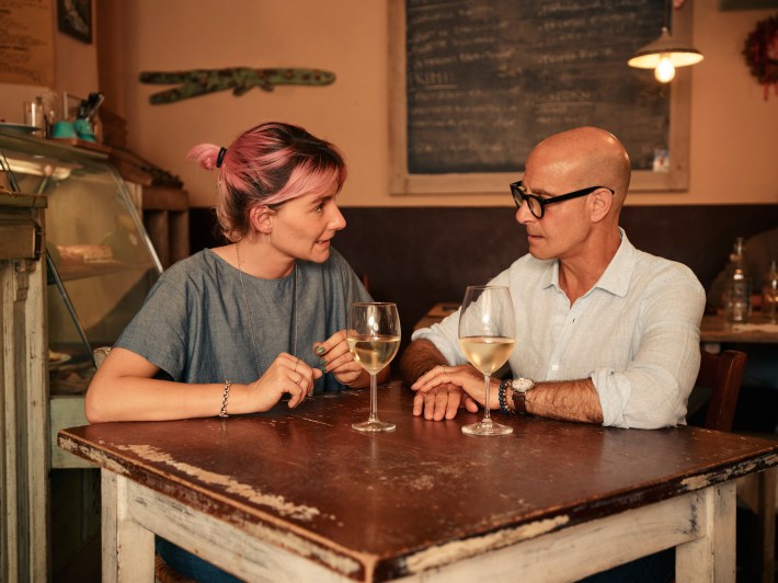 Stanley Tucci conversing with a local woman in a traditional Italian restaurant.