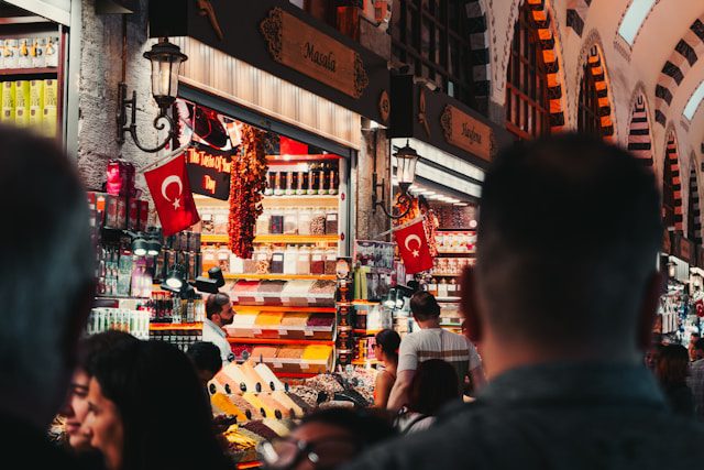 The bustling and brightly lit interior of the Grand Bazaar in Istanbul with ornate lamps hanging from the ceiling.