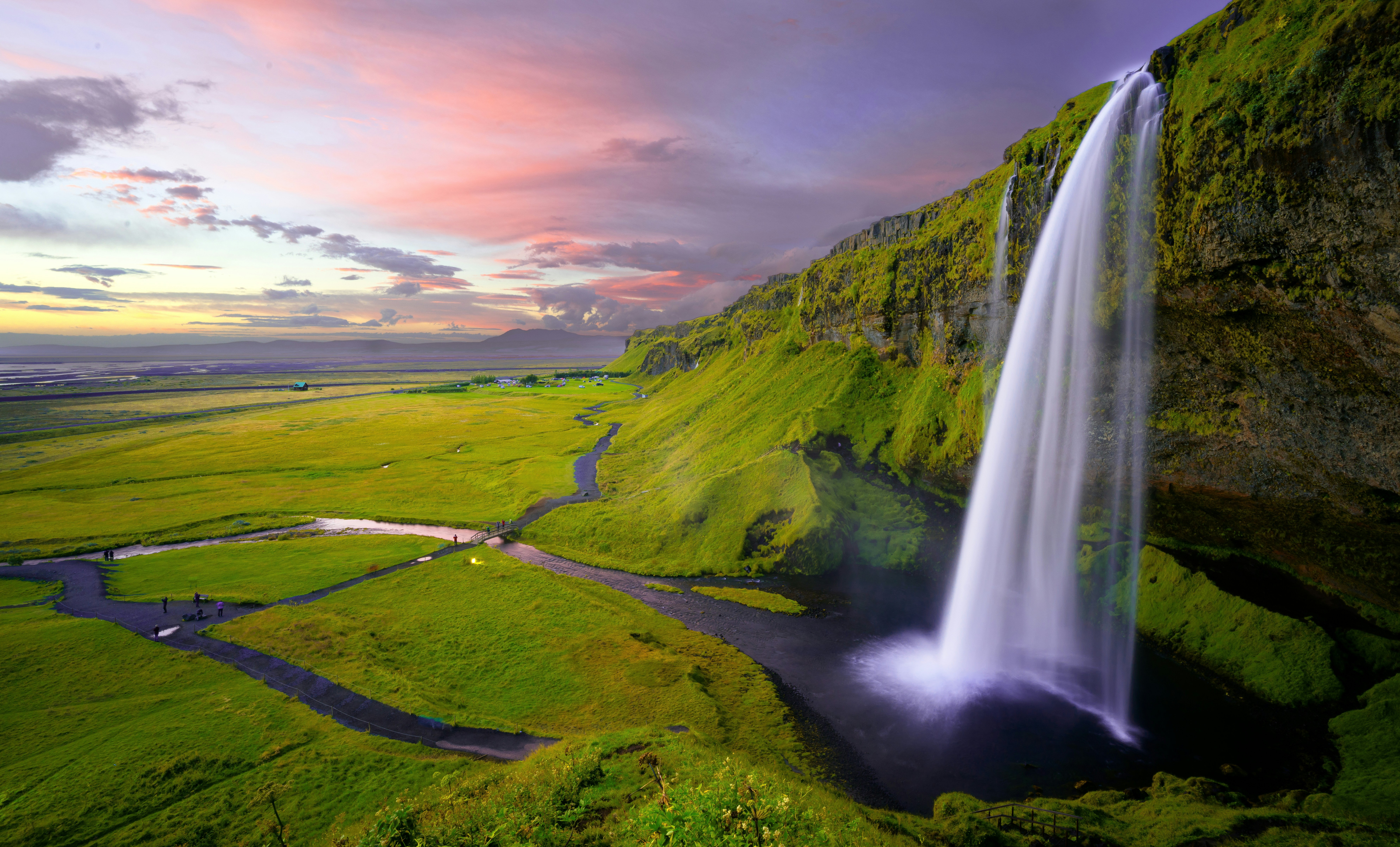 A massive, powerful waterfall cascading down a green cliff in the Icelandic wilderness.