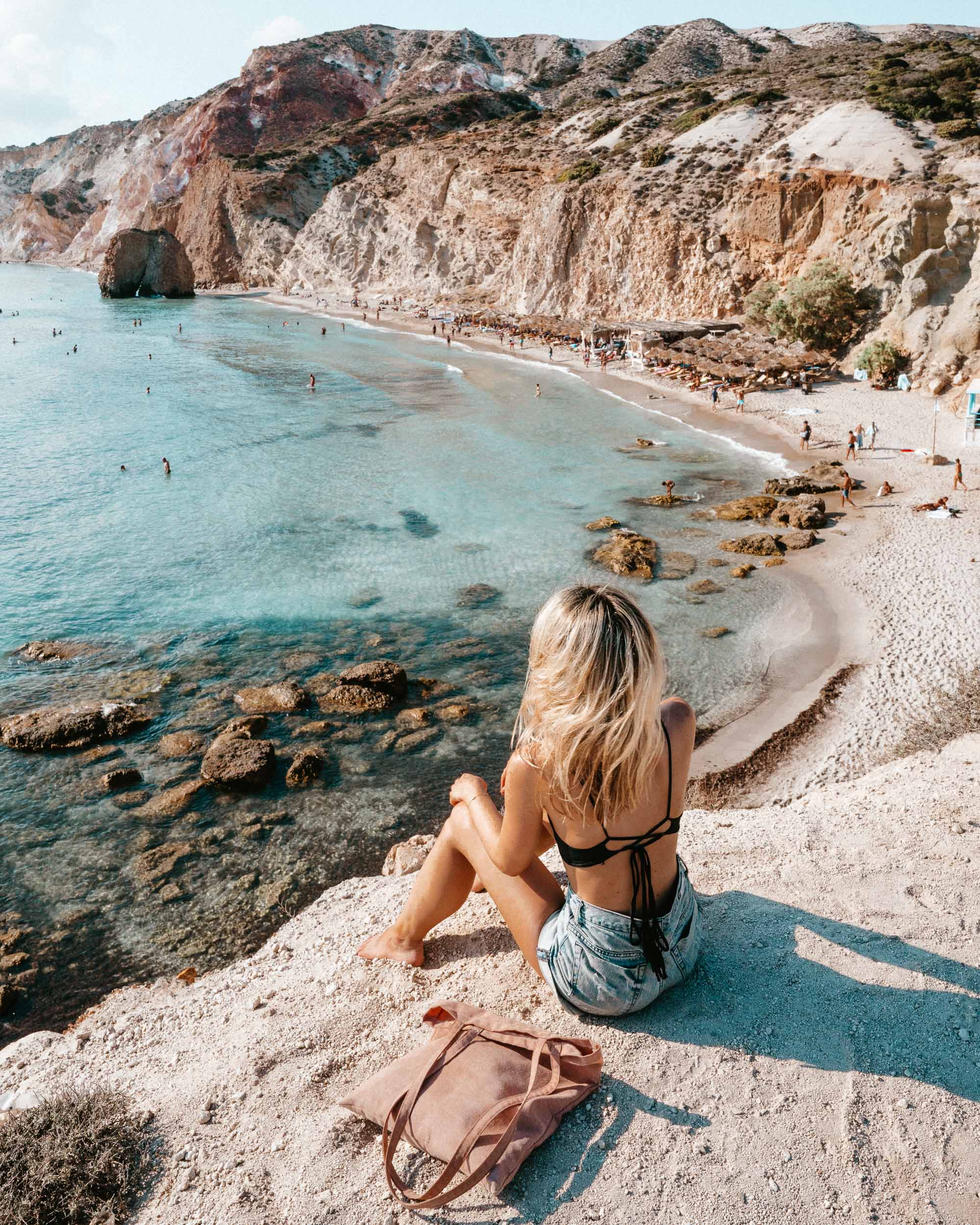 Firiplaka Beach featuring large red volcanic cliffs and a wide sandy shore.
