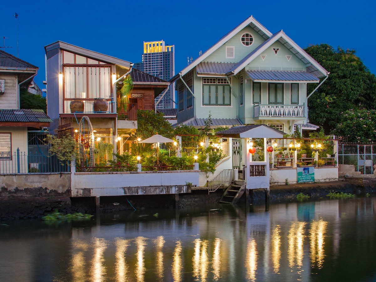 A colonial-style home by a canal illuminated by warm yellow lights at dusk.