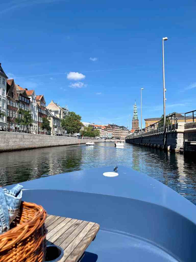 A first-person view from the front of a small boat traveling through a calm city canal.