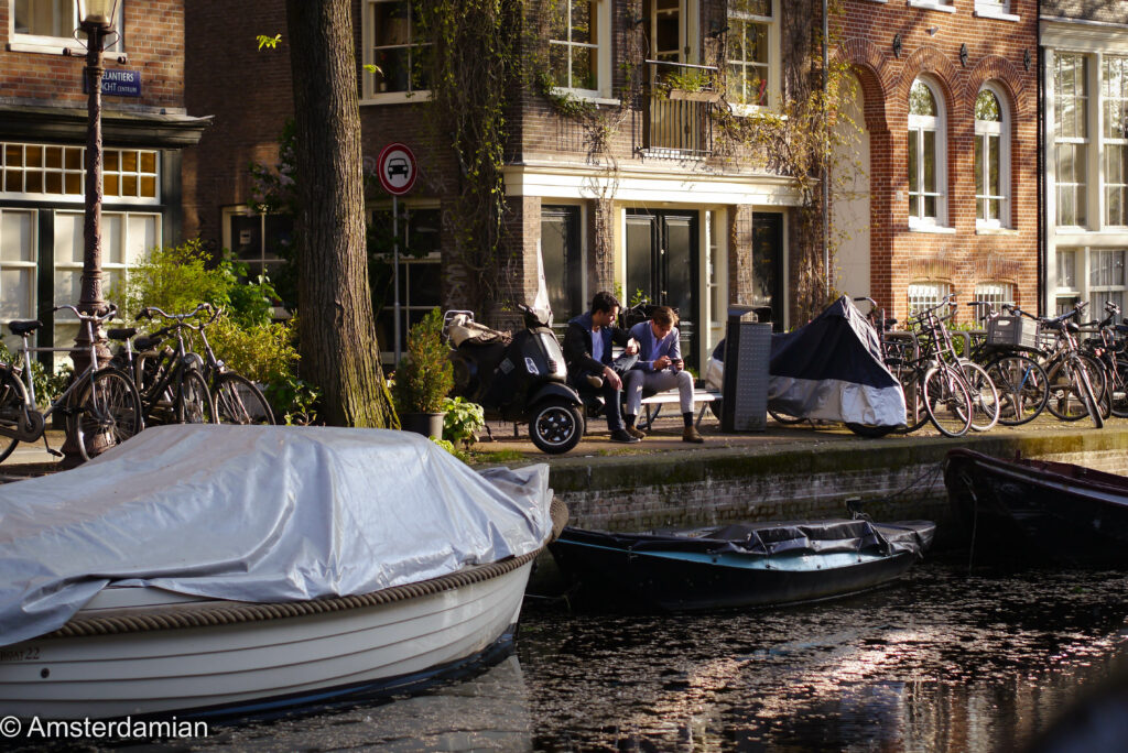 A peaceful view of the Egelantiersgracht canal with houseboats and green trees.