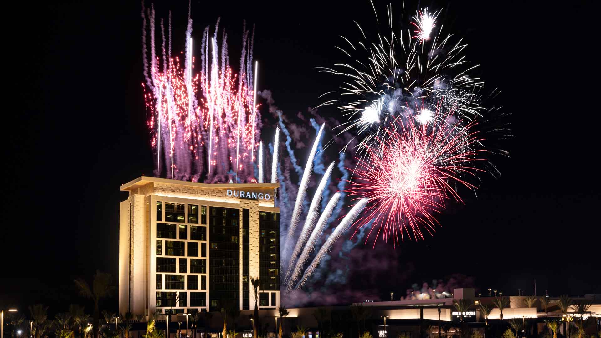 A sky filled with multiple bursts of red and white fireworks over the Las Vegas city skyline.