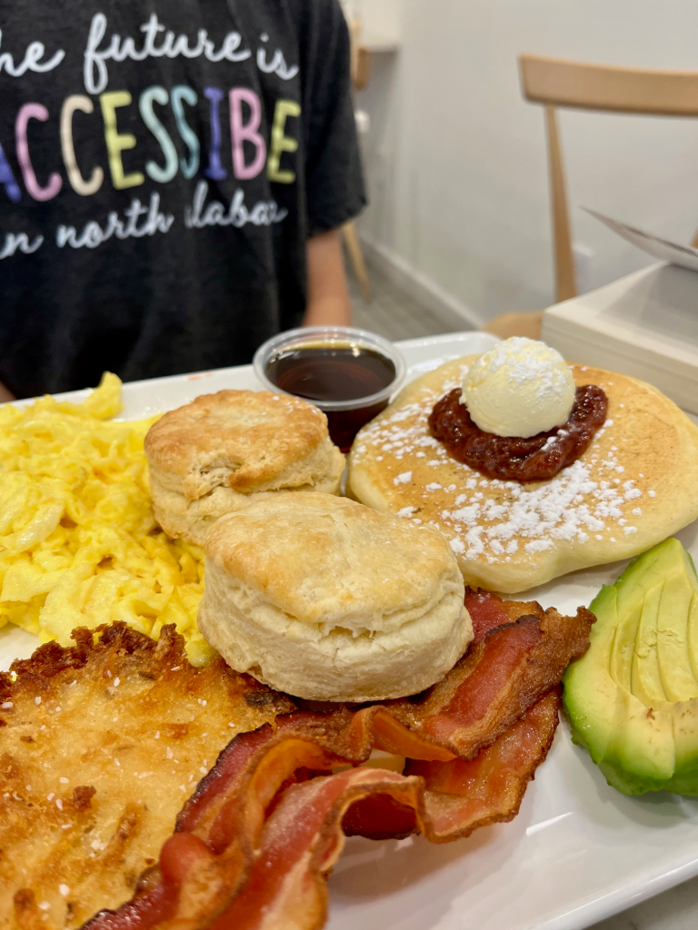 A high-angle shot of a breakfast platter featuring pancakes, eggs, and fruit.