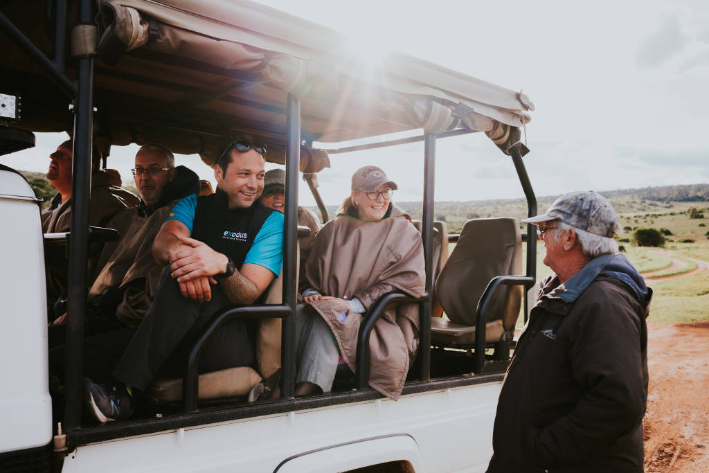 Tourists sitting in an open-top 4x4 safari vehicle in the African savanna.