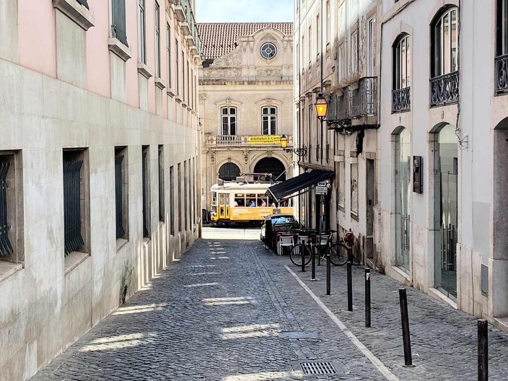 A classic yellow tram navigating a narrow, tiled street in Lisbon, Portugal.