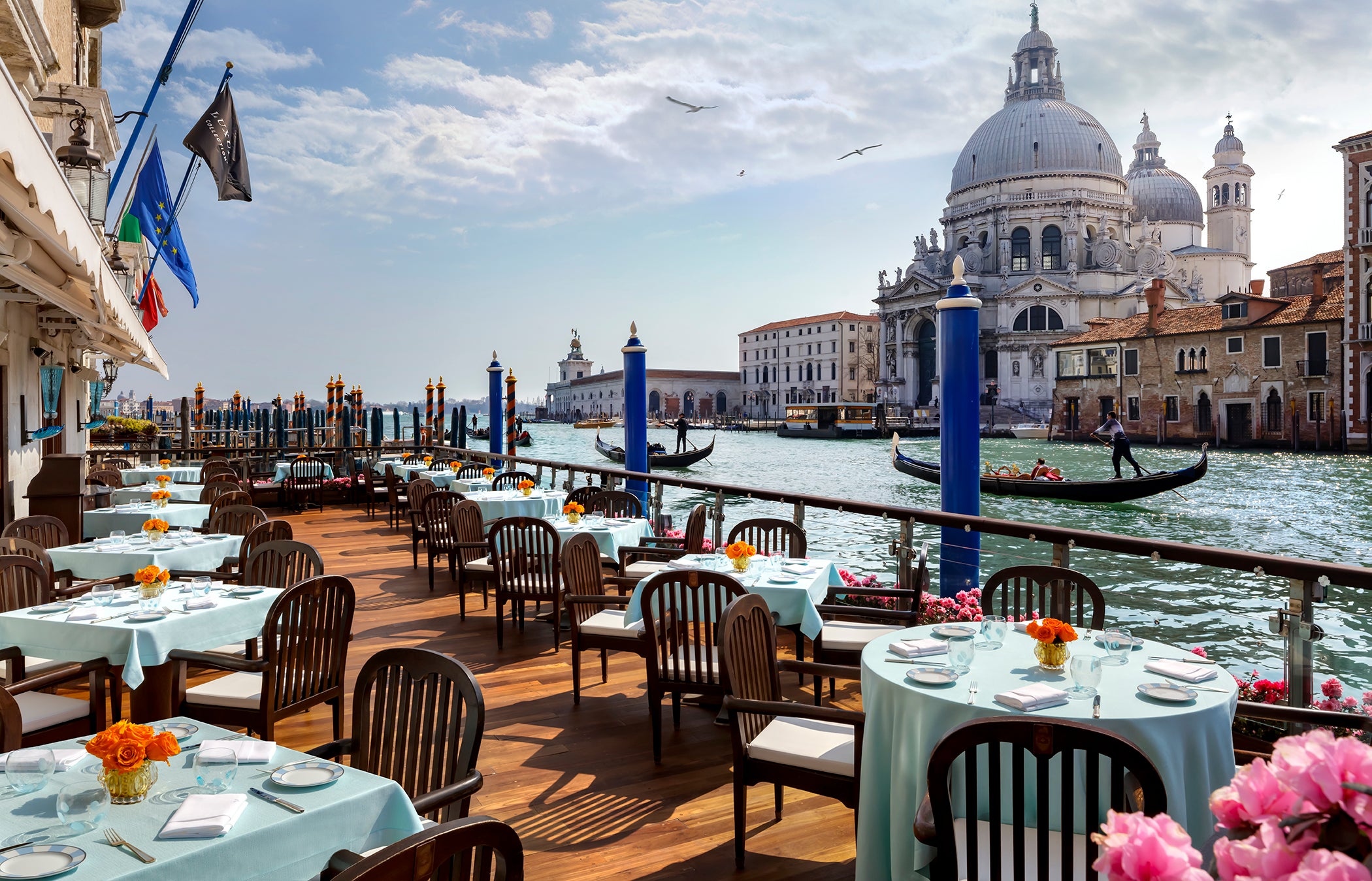 A wide terrace with white tablecloths and classic Venetian chairs overlooking the water and Santa Maria della Salute.