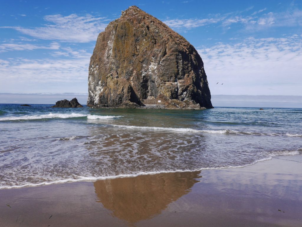 The massive Haystack Rock sea stack standing on the sandy shore of Cannon Beach under a clear sky.
