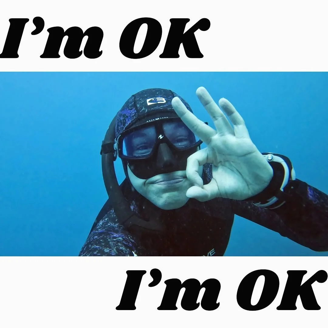 A freediver making the hand signal for 'I am OK' while underwater.