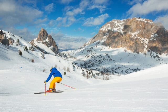 A wide panoramic view of the alpine town of Cortina d'Ampezzo nestled in a valley surrounded by snow-dusted mountains.