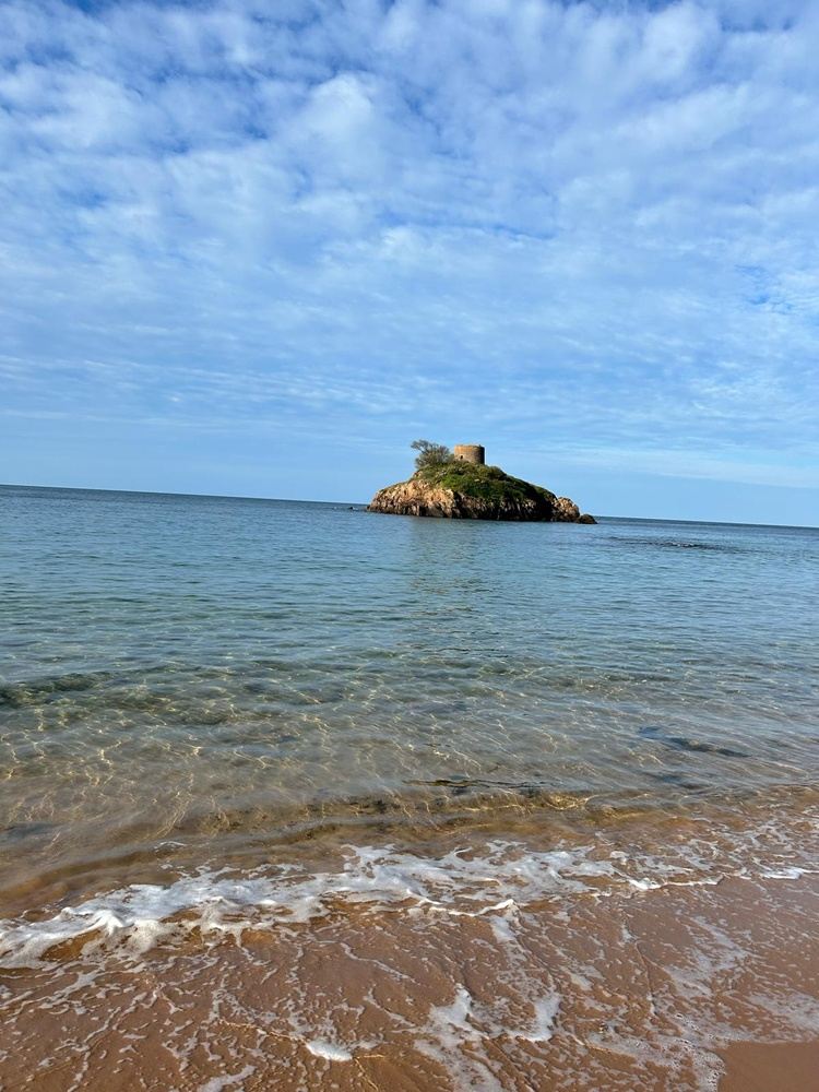 The clear, blue waters and rugged cliffside of the Jersey coast under a sunny sky.
