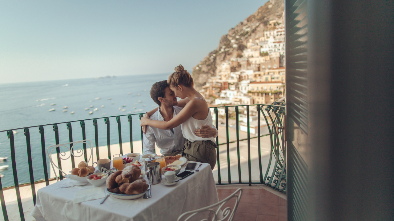 A couple embracing on a traditional Italian stone balcony overlooking a scenic landscape.