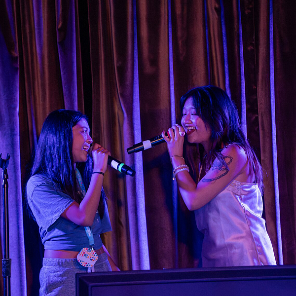 A cruise guest singing enthusiastically on stage during a Broadway-themed karaoke night.