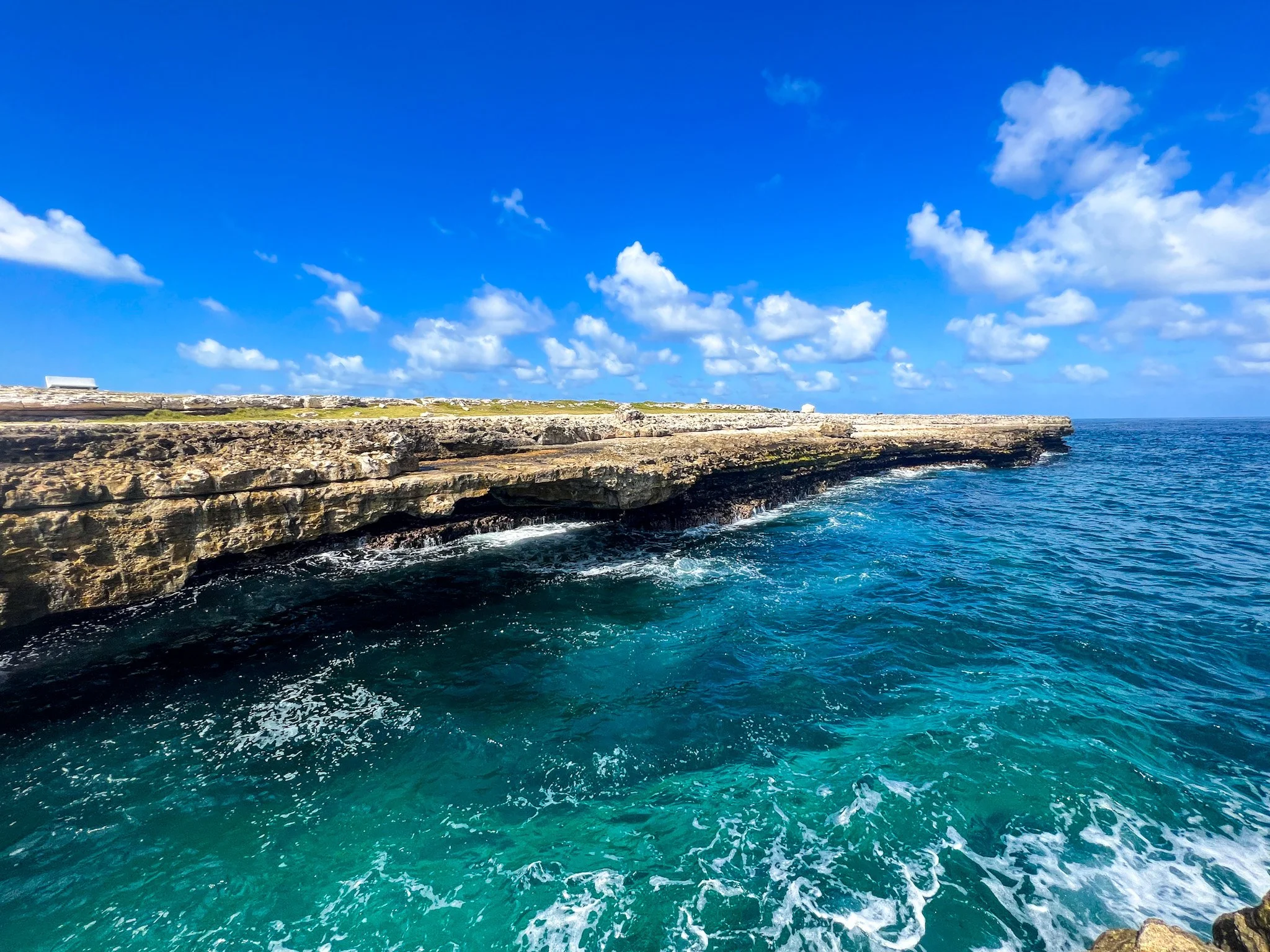 A natural limestone arch formation at Devil's Bridge in Antigua with ocean waves crashing beneath it.