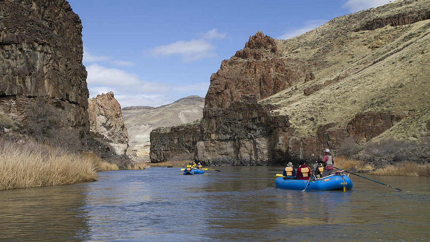Rafts floating through a deep canyon in Eastern Oregon with high rock walls.