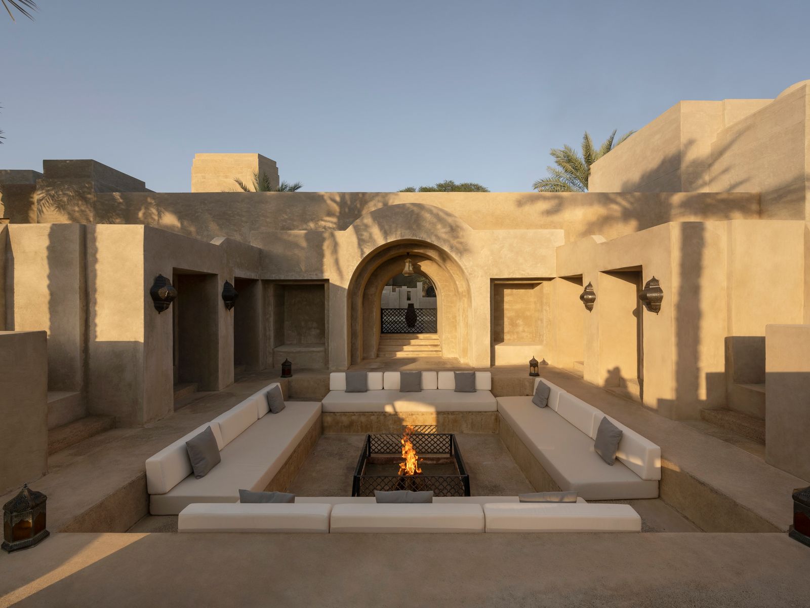 A luxury desert resort fire pit at dusk with sand dunes in the background.