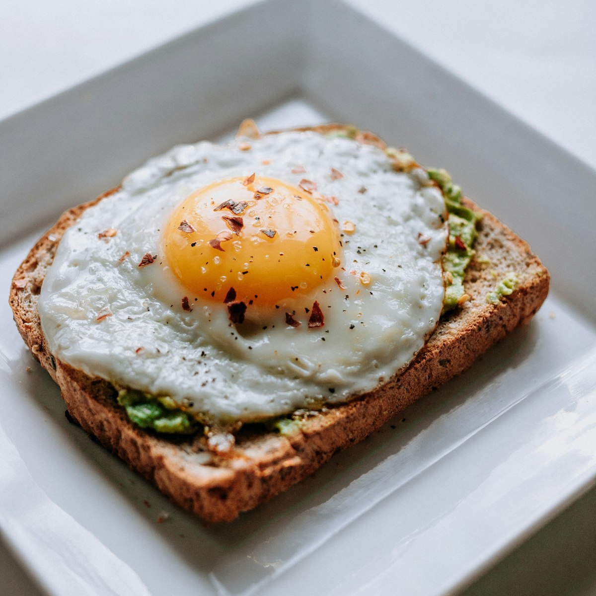 A plate of fresh avocado toast served with tropical fruit and eggs on a table.