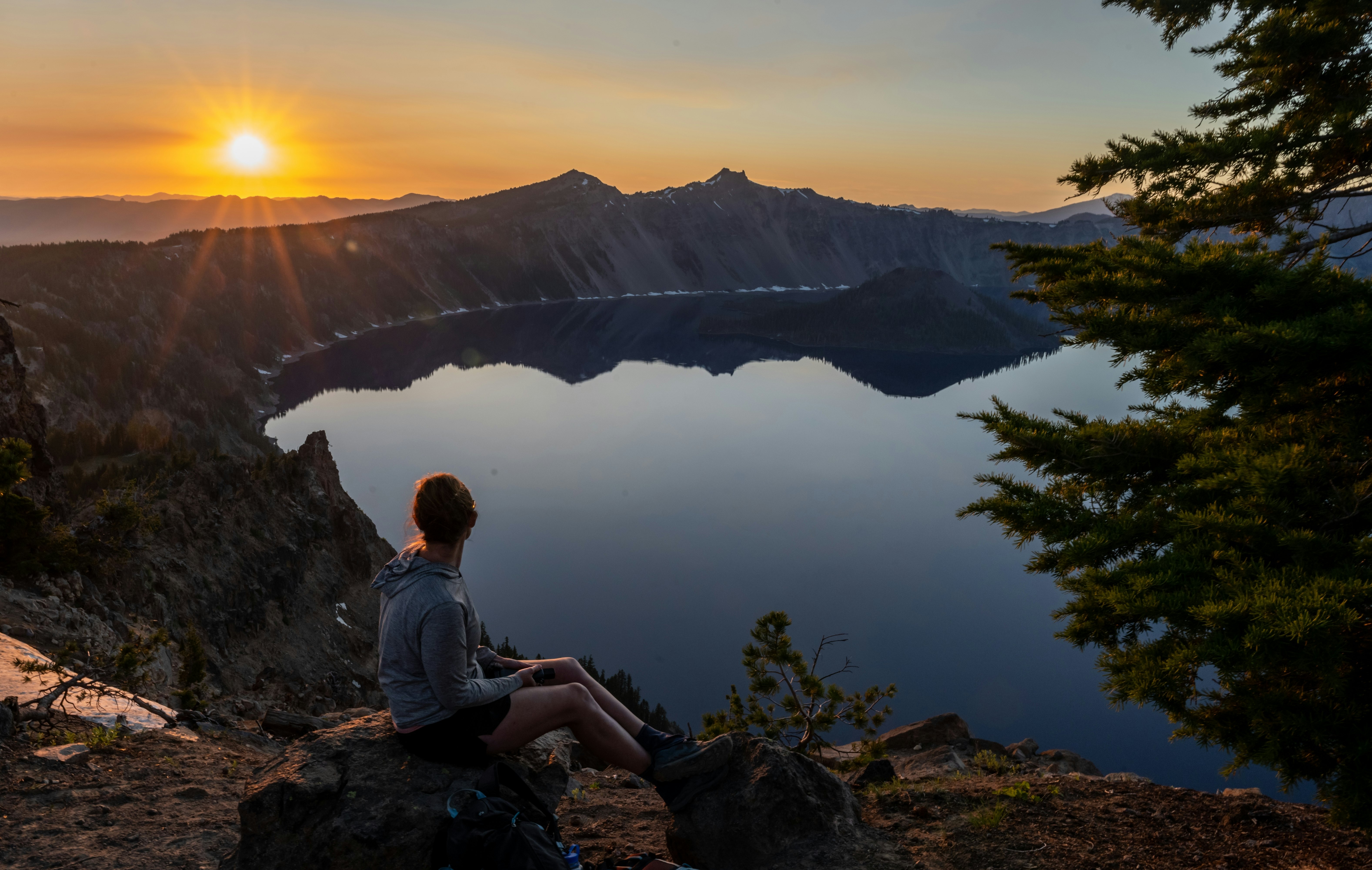 A person sitting on a rocky ledge at Garfield Peak watching the sun set over the blue lake.