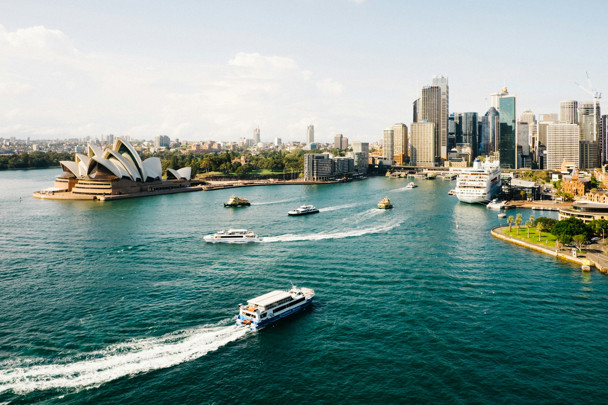 The Sydney Opera House and the city skyline illuminated at sunset by the harbor.