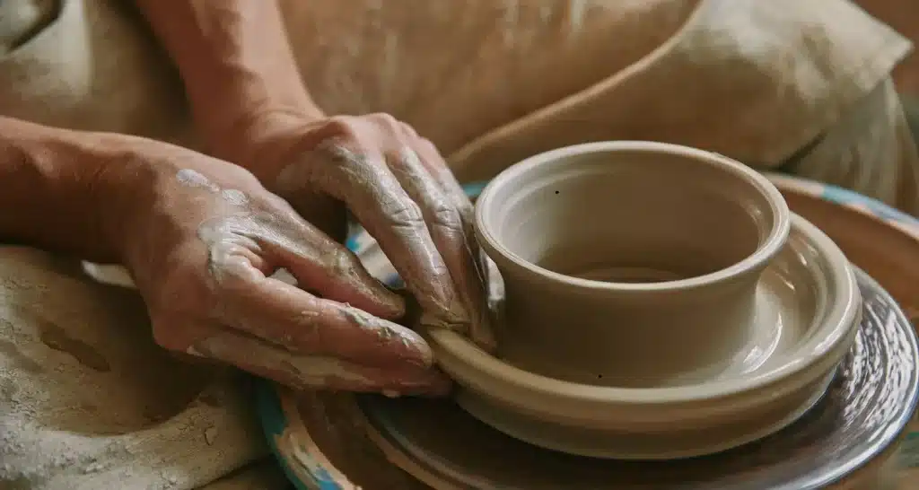 Detailed close-up of a craftsman's hands shaping a clay pot on a pottery wheel.